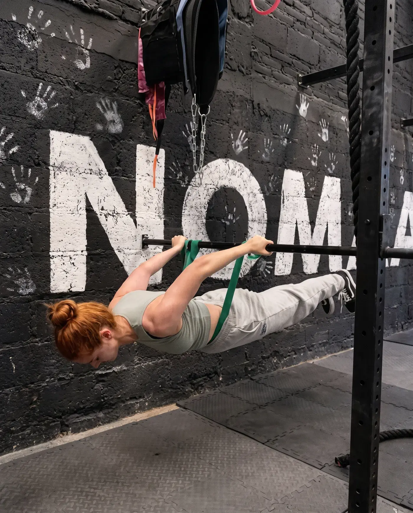 Alumna sosteniendo un front lever con liga frente al muro de Nómada